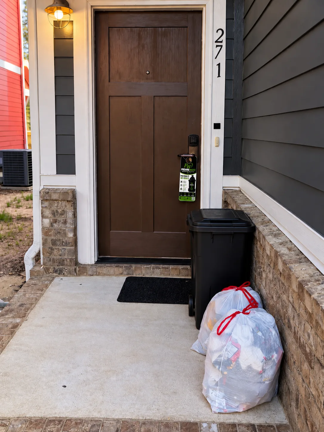 Apartment doorway with a black trash container, tied trash bags, and a Premium Waste door hanger