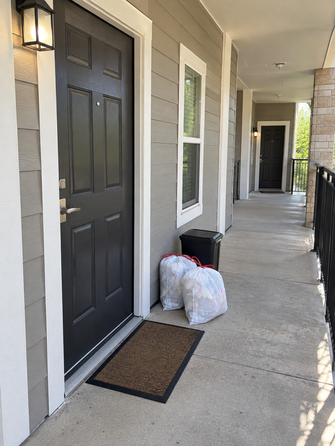 Two securely tied trash bags placed beside an apartment door in daylight